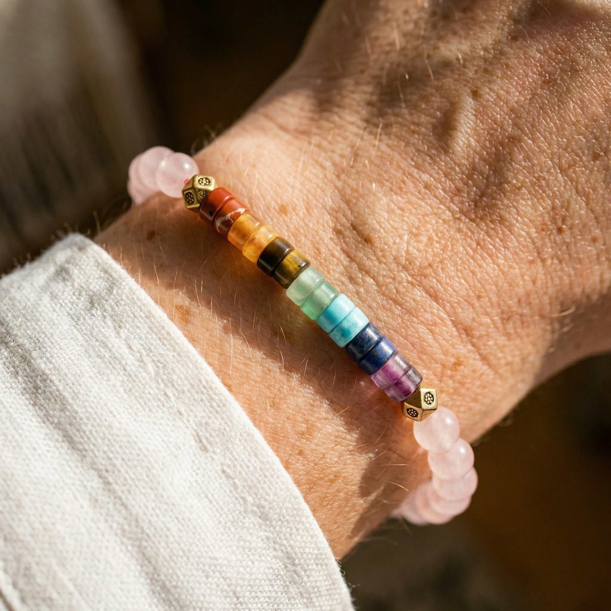 Bransoletka z kwarcu różowego i 7 kamieni czakr na nadgarstku. Kolorowa biżuteria naturalna w stylu boho.