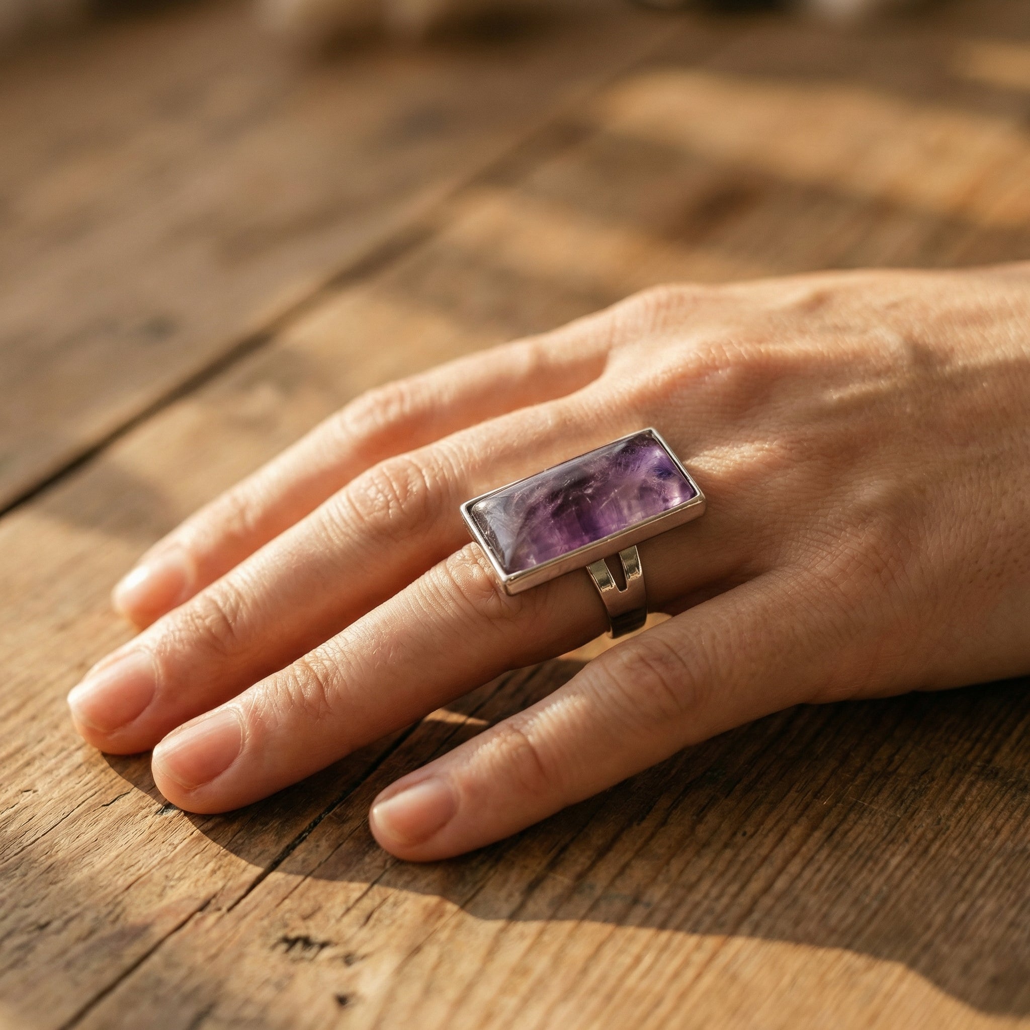 Regulowany srebrny pierścionek z dużym prostokątnym ametystem naturalnym na dłoni.