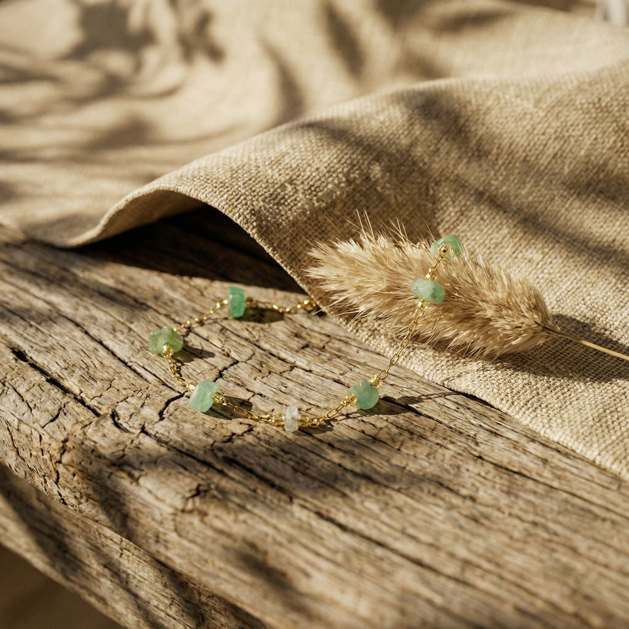 Elegancka bransoletka z naturalnym zielonym awenturynem i złotym łańcuszkiem na rustykalnym tle.