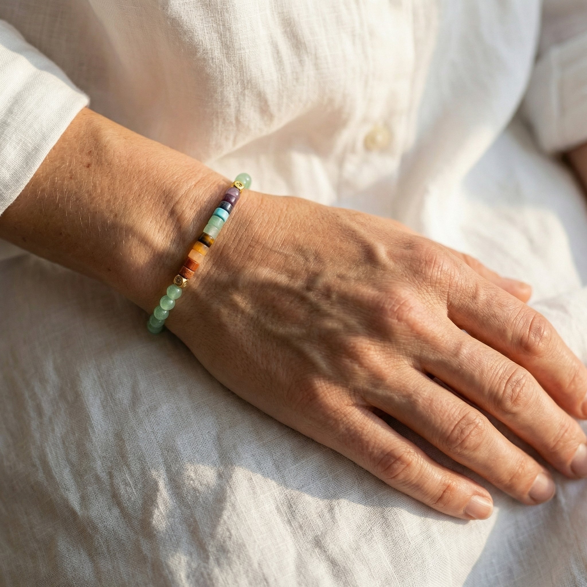 Bransoletka z zielonym awenturynem i kamieniami 7 czakr 4mm na ręce modelki w białej lnianej koszuli.